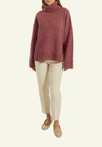 Rosa Strickpullover mit hohem Rollkragen, weiten Ärmeln und gerippten Bündchen, kombiniert mit cremefarbenen Stoffhosen und beigen Slippern.