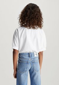Maglietta bianca a maniche corte con risvolti, abbinata a jeans in denim azzurro chiaro a vita alta con etichetta sul retro.