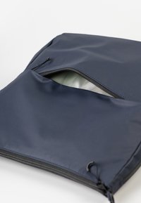 Dunkelblaues, mit Reißverschluss versehenes Täschchen aus glattem, wasserdichtem Material; verfügt über eine teilweise Öffnung, die ein helles Innenfutter offenbart.