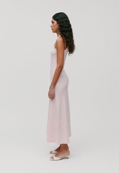 Lang roze mouwloos jurkje met een aansluitende silhouette, gemaakt van zachte stof, met een rechte zoom. Gecombineerd met witte open-teen hakken.