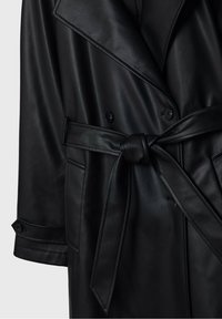 Trench-coat noir en similicuir avec larges revers, boutons croisés, poches latérales, taille ceinturée nouée et poignets de manches boutonnés.