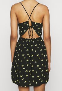 Černé květinové šaty se žlutými vzory citronů, výřezem na zadní straně, stahovacími detaily, nastavitelními tenkými ramínky a uvolněným střihem.