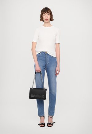 Camicetta bianca a maniche corte, jeans blu a vita alta, borsa nera con tracolla a catena e sandali neri con dettaglio a fiocco. Design e colori semplici.