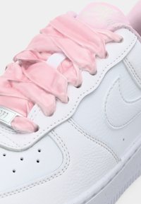 Sneaker in pelle bianca con lacci in satin rosa. Presenta un'etichetta di branding argentata e un pannello laterale testurizzato, che mette in mostra il design del logo Nike.