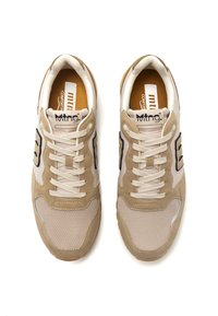 Zapatillas beige que combinan materiales de ante, malla y goma. Diseño de cordones con acentos en negro contrastantes y marca.