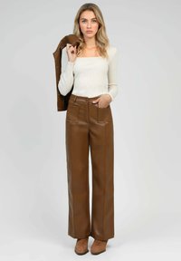 Pantalons larges en simili cuir marron avec poches avant, associés à un haut à manches longues côtelé couleur crème clair. Modèle tenant une veste assortie.