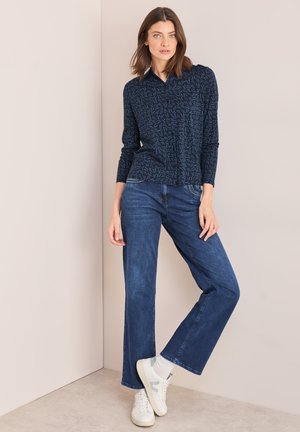 Chemise boutonnée à motif marine avec des manches longues, associée à un jean droit bleu foncé et des baskets blanches. Tissu lisse, coupe décontractée.