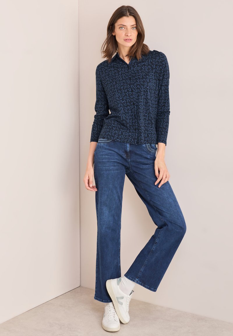Camicia a bottoni a maniche lunghe con motivo navale, abbinata a jeans dritti blu scuro e sneakers bianche. Tessuto morbido, vestibilità rilassata.