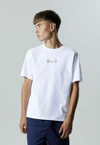 Hvid bomulds t-shirt med et grafik af tre citrusfrugter: en citron, en lime og en orange, centreret på brystet. Korte ærmer, rund hals.