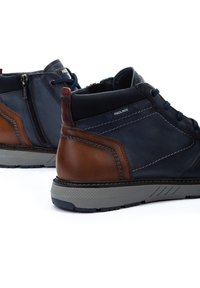 Botas de tobillo para hombre en piel azul marino con acentos marrones, con un acabado texturizado, costuras en contraste y una suela de goma con un patrón de relieve.