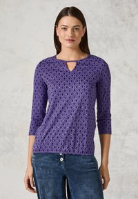 Violetti pitkähihainen paita, jossa on timanttikuosi, pyöreä kaula-aukko avainreiällä, yhdistettynä sinisiin farkkuihin. Pehmeä kangas, rento malli.