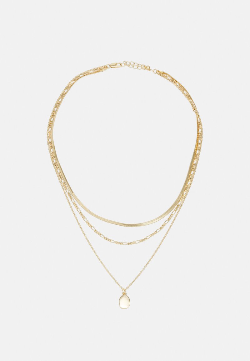 Guldtonet lagdelt halskæde med flere kæder i varierende tykkelse, hvoraf den ene har en lille oval charm. Inkluderer glatte og teksturerede elementer.