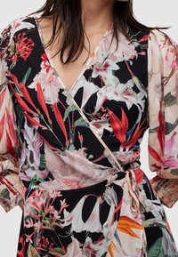 Robe portefeuille florale mettant en valeur un fond noir orné de fleurs colorées dans des nuances de rouge, rose et vert. Manches transparentes et texturées avec un détail à nouer.