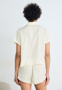 Chemise courte, de couleur jaune pâle, à manches courtes et avec un col, associée à un short assorti. Les deux pièces sont en tissu léger et lisse.