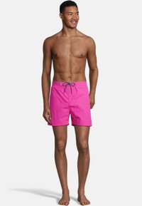 Shorts de bain rose vif avec une fermeture à cordon. Fabriqués en tissu léger, ils présentent une texture lisse et des accents verts à l'intérieur.