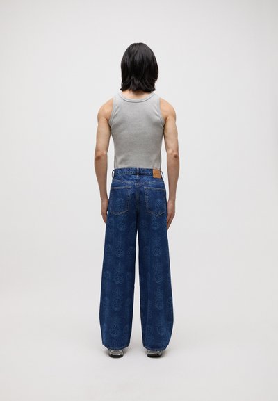 Pantalons en denim à larges jambes de couleur bleu foncé avec un motif floral, associés à un haut sans manches gris. Détails rayés sur le jean.