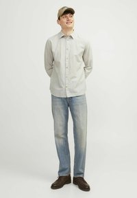 Camicetta grigio chiaro a maniche lunghe con un motivo sottile, abbinata a jeans dritti blu sbiaditi e scarpe marroni, completata da un cappellino beige.