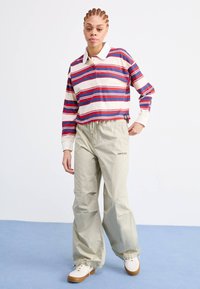 Rutet langermet polo i kremfarge, rød og blå med krage, matchet med lysebeige bukser med elastisk hem og rødt logo.