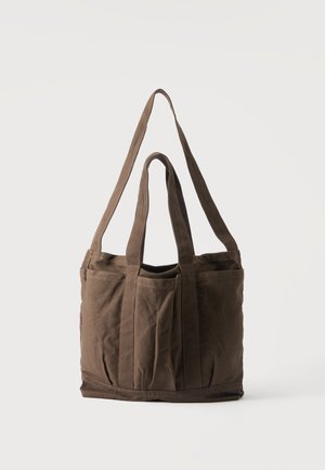 Borsa tote in tela marrone con due manici corti e uno lungo, con tasche esterne, su sfondo chiaro uniforme.