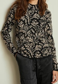 Maglione nero con un motivo floreale crema, dotato di maniche lunghe e scollatura alta. Texture morbida e design aderente.