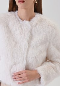 Weiße Kunstpelzjacke mit weicher Textur, rundem Halsausschnitt und dreiviertellangen Ärmeln. Minimalistisches Design ohne sichtbare Beschläge.