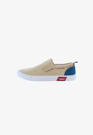 Zapato de lona tipo slip-on en beige con acento azul marino. Suela de goma blanca. Presenta texto de logo rojo a lo largo del lado y una pequeña etiqueta roja en el talón.