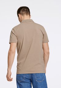 Polo shirt beige con colletto e maniche corte, indossato con jeans in denim blu. Texture liscia con dettagli minimi.