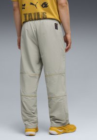 Lysegrå sportsbukser med elastisk talje, gul syning og afslappet pasform, parret med gule sneakers og en grafisk t-shirt.