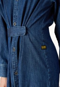 Robe chemise en denim bleu foncé, dotée d'une taille nouée, de manches longues, d'une fermeture par boutons et d'une étiquette logo G-Star Originals sur le côté.