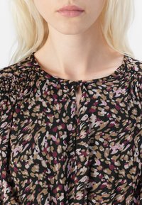 Svart blus med blommönster i rosa, beige och brunt. Har en nyckelhalsringning och rynkdetaljer vid axlarna.