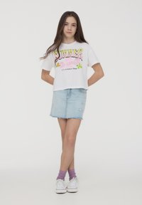 T-shirt bianco cropped con grafica colorata "SUMMER LOS ANGELES", abbinato a una gonna di jeans azzurro chiaro con dettagli strappati.