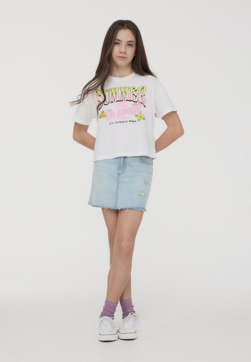 T-shirt bianco cropped con grafica colorata "SUMMER LOS ANGELES", abbinato a una gonna di jeans azzurro chiaro con dettagli strappati.