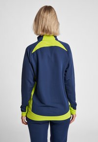 Granatowa kurtka sportowa z wysokim kołnierzem, z jaskrawymi akcentami w kolorze limonki. Teksturowany materiał z kropeczkowym wzorem na rękawach.