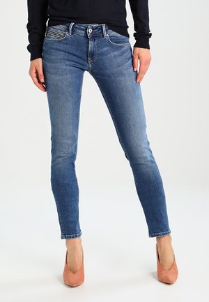 Štíhlé modré džíny ze sevřeného denimu s vybledlým praním, designem s pěti kapsami a zapínáním na knoflík. V kombinaci se světle růžovými lodičkami.