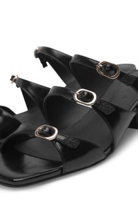 Black sandals featuring a smooth leather finish, cross straps, gold-tone hardware accents, and a square toe shape.