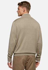 Maglione beige a maglia con colletto alto e texture a coste, con maniche lunghe e una vestibilità morbida. Abbinato a pantaloni marrone chiaro.