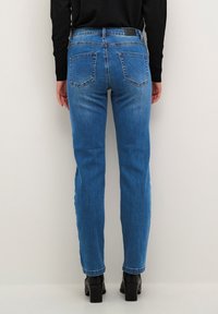 Ljust blå denimjeans med rak passform, bakfickor och en svart midjebandsetikett, kombinerat med svarta högklackade stövlar.