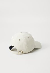 Căciulă de baseball din fâșie albă, cu o margine curbă, orificii de ventilație și o curea reglabilă pe spate cu elemente metalice.