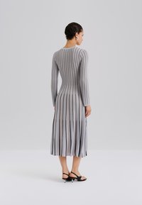 Długa, prążkowana sukienka w jasnoszarym kolorze z pionowymi paskami w ciemnoszarym i brzoskwiniowym odcieniu. Dopasowana sylwetka, długie rękawy i rozkloszowany dół.