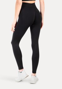 Zwarte high-waisted leggings met een textuurpatroon, strakke pasvorm; gecombineerd met lichtgrijze sportschoenen met een kousachtige hals.