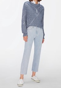 Modrý pletený svetr s texturovaným vzorem, zkombinovaný se světle modrými rovnými džíny a bílými teniskami s černými akcenty.