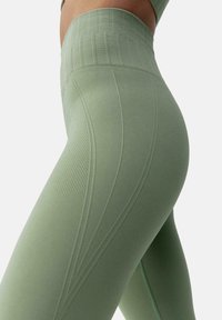 Høyt midjebelte, lysegrønne leggings laget av teksturert stoff med ribbet midjebånd og skrå sømdetaljer for en tettsittende silhuett.