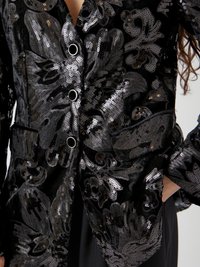 Blazer noir pailleté avec motif floral, composé de paillettes noires et argentées brillantes, deux poches avant et boutons ronds en métal.