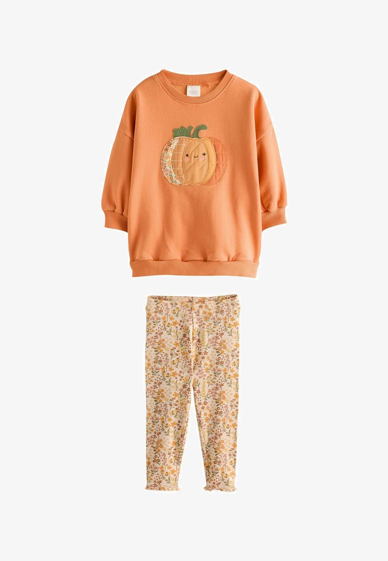 Sudadera naranja de manga larga para niño pequeño con un diseño de calabaza sonriente, combinada con leggings beige con estampado floral.