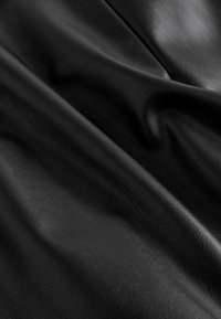 Musta, teksturoitu nahkamateriaali, jossa on sileä pinta, pehmeitä poimuja ja korostuksia, jotka korostavat sen notkeaa laatua.