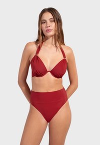 Crvene bikini visokog struka s dubokim dekolteom, izrađen od glatkog materijala, s zlatnim detaljima na trakama.