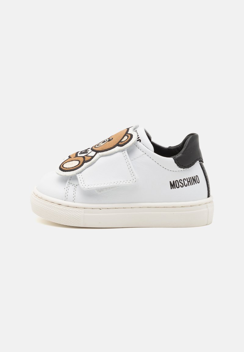 Sneaker in pelle bianca con un accento nero sul tallone e un grande design di orso teddy sul cinturino. Nome del marchio "MOSCHINO" stampato sul tallone.
