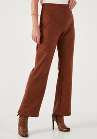 Braune, weit geschnittene Hosen aus weichem Stoff mit glatter Textur und hohem Taillenbund. Zusätzliche Details sind ein dezentes Saumdesign.