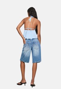 Top corto azzurro con collo a halter, adornato da un volant arricciato e chiusura a lacci, abbinato a pantaloni corti di jeans blu di lunghezza media con tasche posteriori.