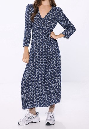 Mørkeblå mønstret maxikjole med lange ærmer, V-hals og taljesmøring, kombineret med hvide sneakers og beige ankelstrømper.